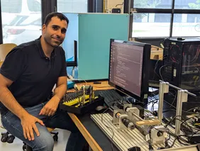 Mühenad Bilal in the lab (Photo: THI). mann an einem Schreibtisch, der mit einem Set aus verschiedenen Bohrern vor einem Bildschirm sitzt, neben ihm eine Bohrvorrichtung