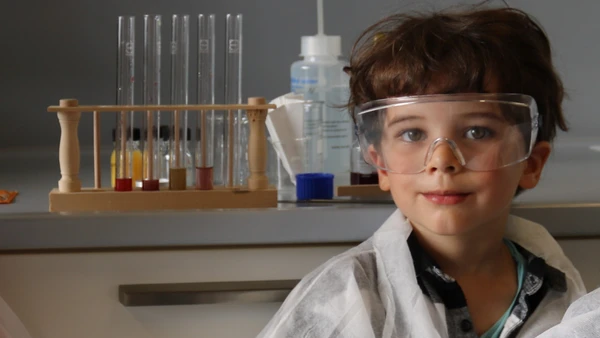 Wie ein richtiger Wissenschaftler: Der 5-jährige Vincent im Labor (Foto: THI). KiGa-Kind in einem Labor mit Schutzbrille und -Kleidung, im Hintergrund Reagenzgläser