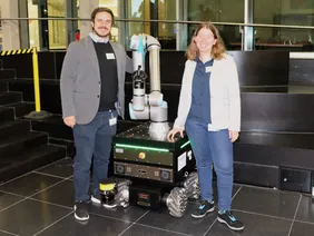 R10D10: Der smarte Roboter kann selbständig aufräumen (Foto: THI). Zwei Personen mit Roboter
